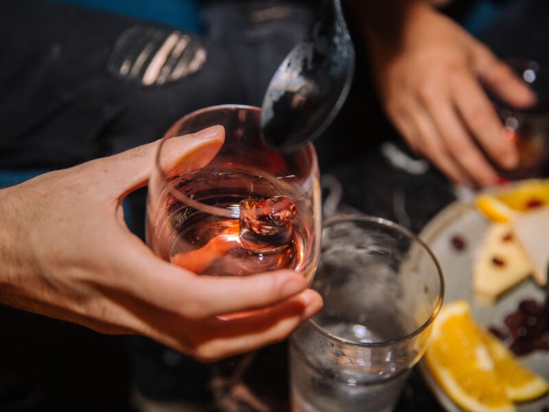 Hand holding a clear containing a light orange spirit and single ice cube